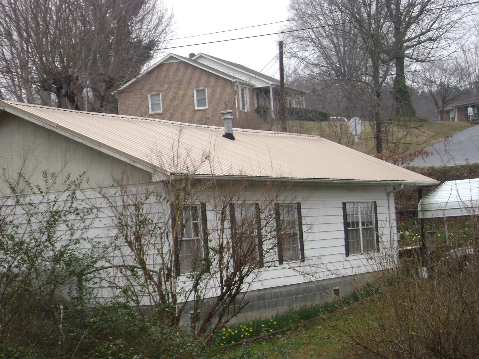 Tan metal roof on a white sided house set into a hillside — Commercial Roofing by Roofing Brothers in Mount Vernon